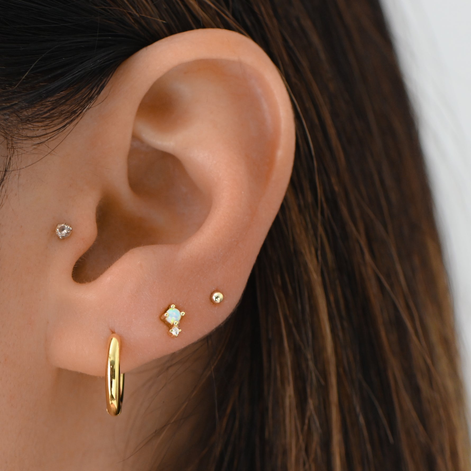 Model wearing gorgeous gold dainty hoop earrings paired with opal cz stud earrings and simple ball studs. 