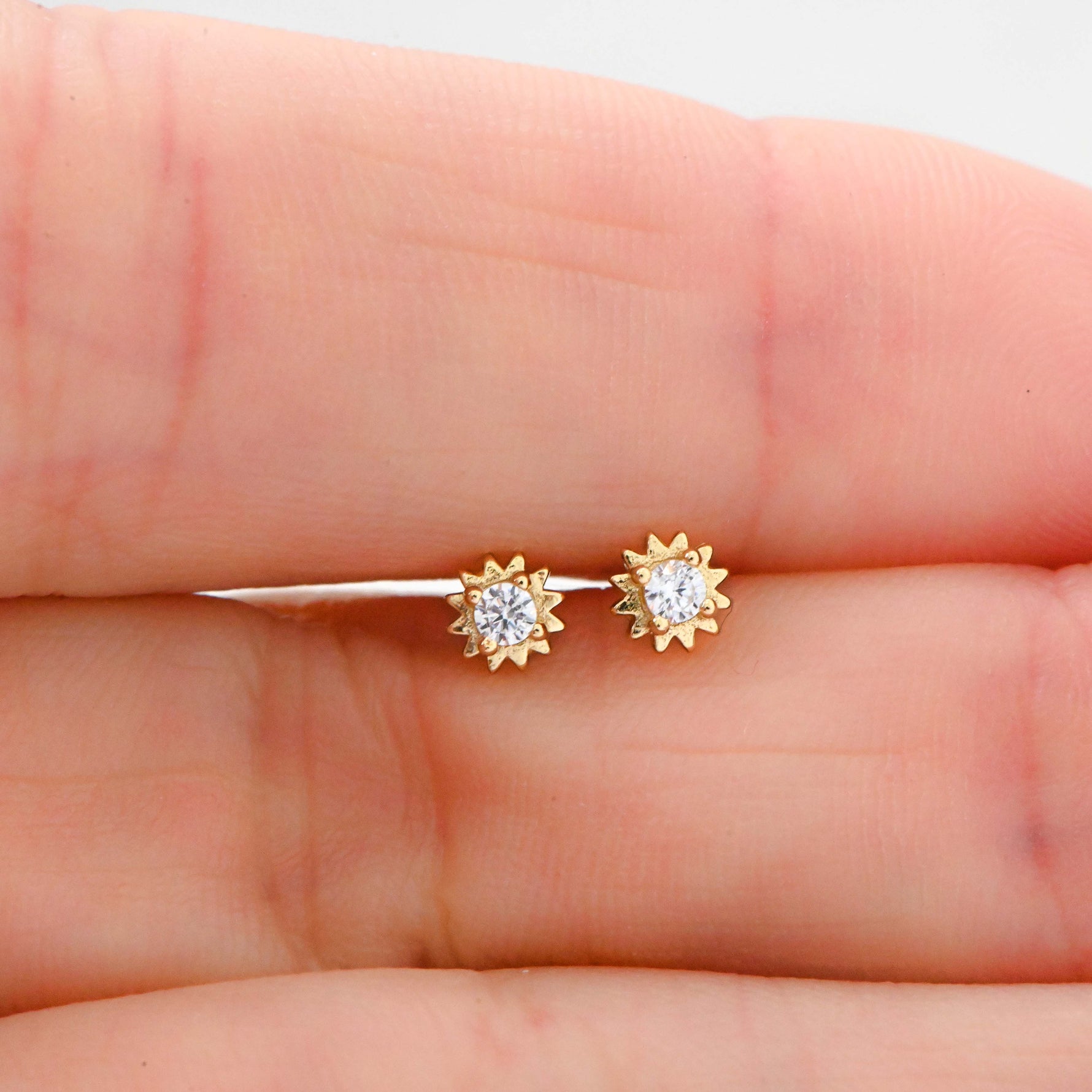 Model holding delicate gold sunburst stud earrings. 