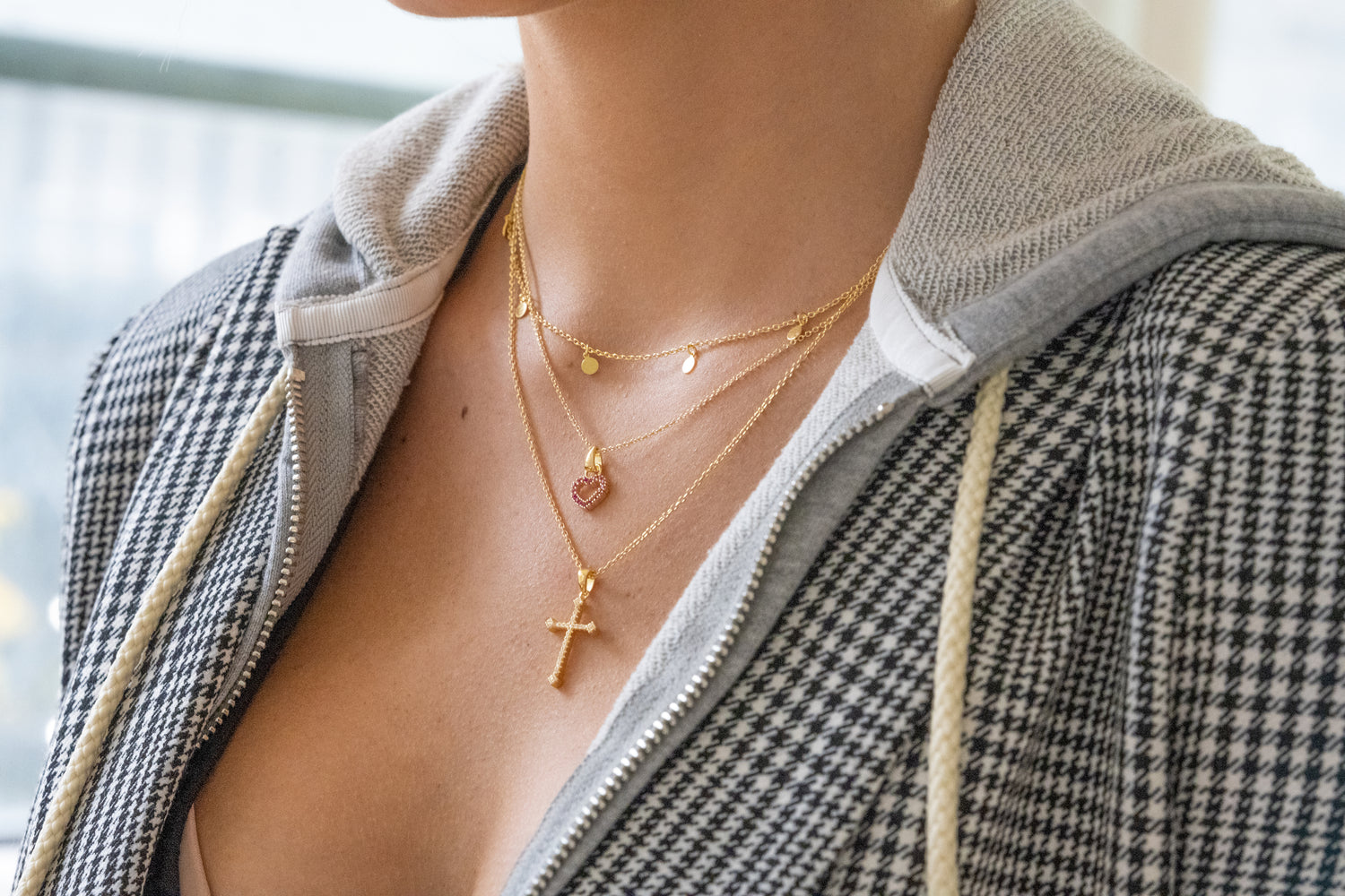 Model wearing gold charm necklace, heart pendant necklace, and cz cross pendant necklace.
