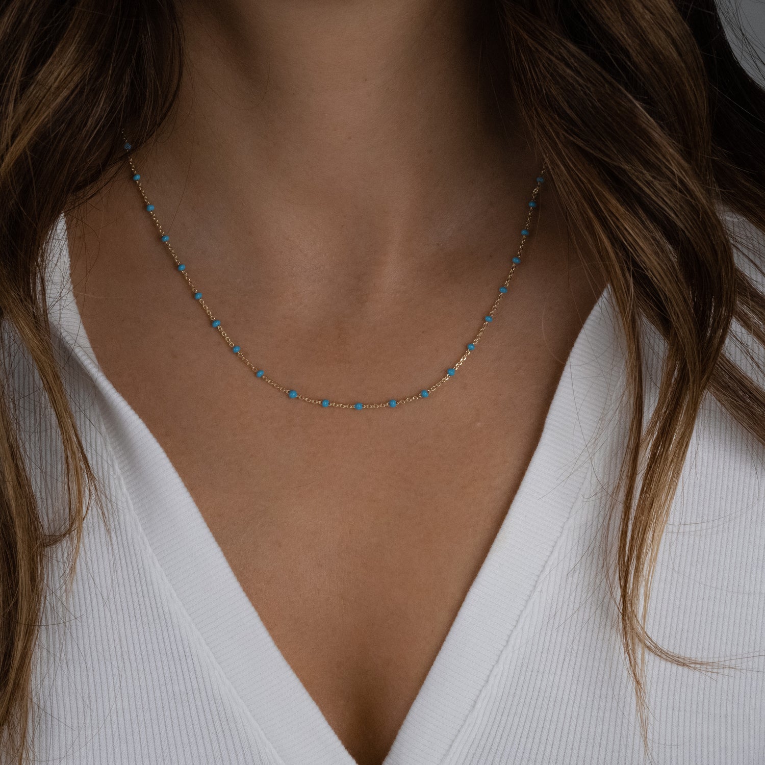 Model wearing minimalist turquoise beaded enamel necklace with a delicate gold chain.