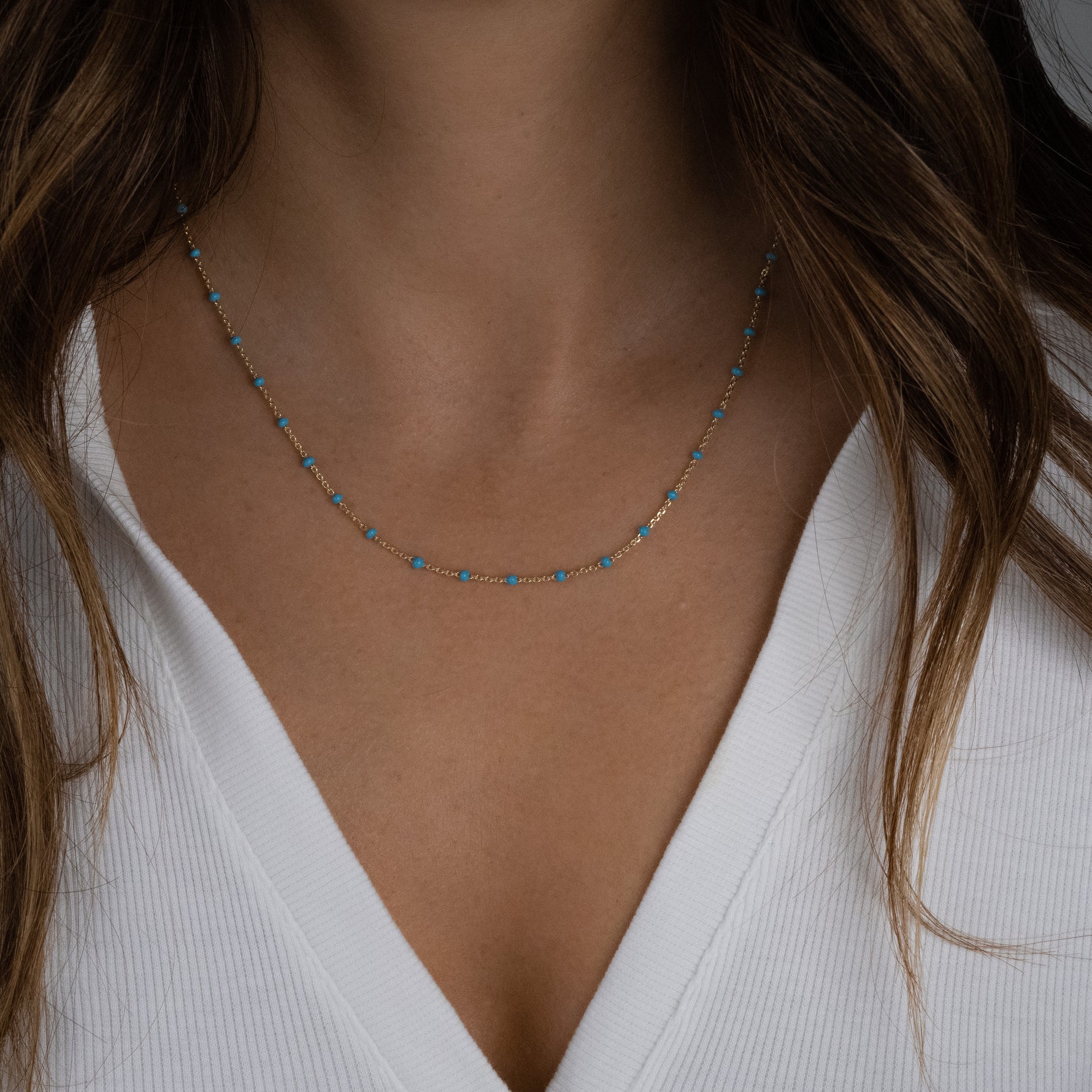 Model wearing minimalist turquoise beaded enamel necklace with a delicate gold chain.