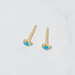 Vibrant gold turquoise round stud earrings from the top angle on marble background.