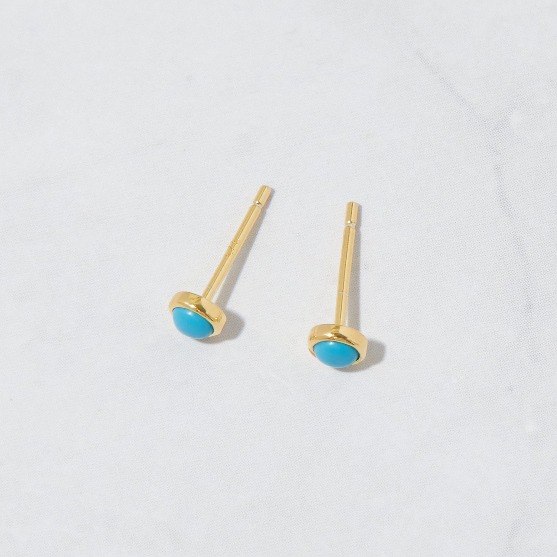 Vibrant gold turquoise round stud earrings from the top angle on marble background.