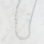 Silver tennis and paperclip chain necklace on marble background.