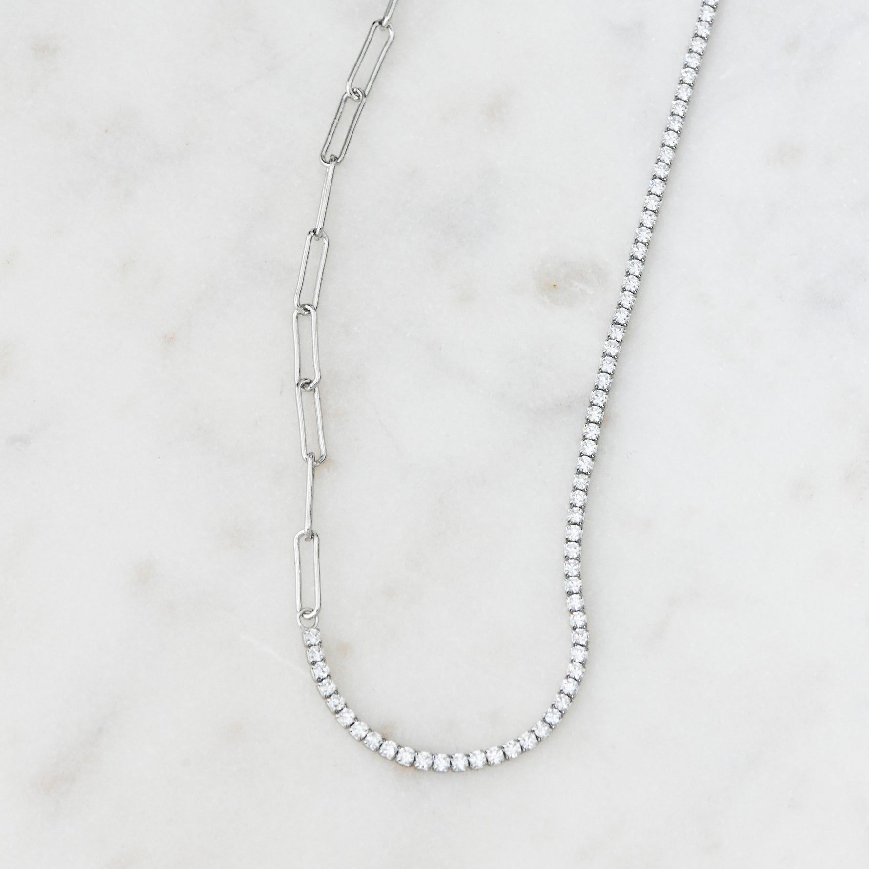 Silver tennis and paperclip chain necklace on marble background.