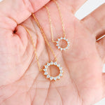 Close-up of dainty sunburst pendant with cubic zirconia stone on models hand