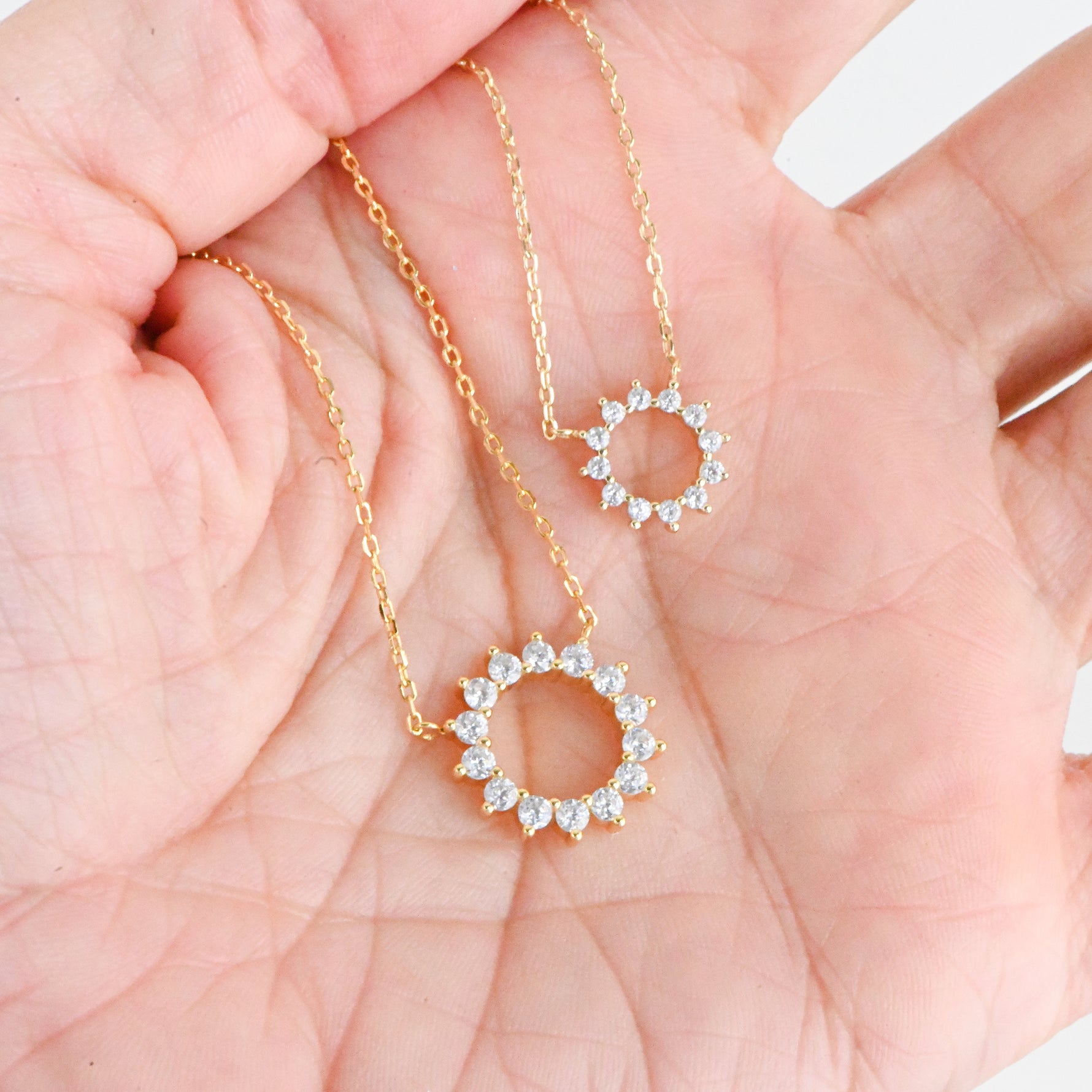 Close-up of dainty sunburst pendant with cubic zirconia stone on models hand