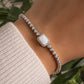 model wearing silver diamond tennis bracelet with opal halo charm