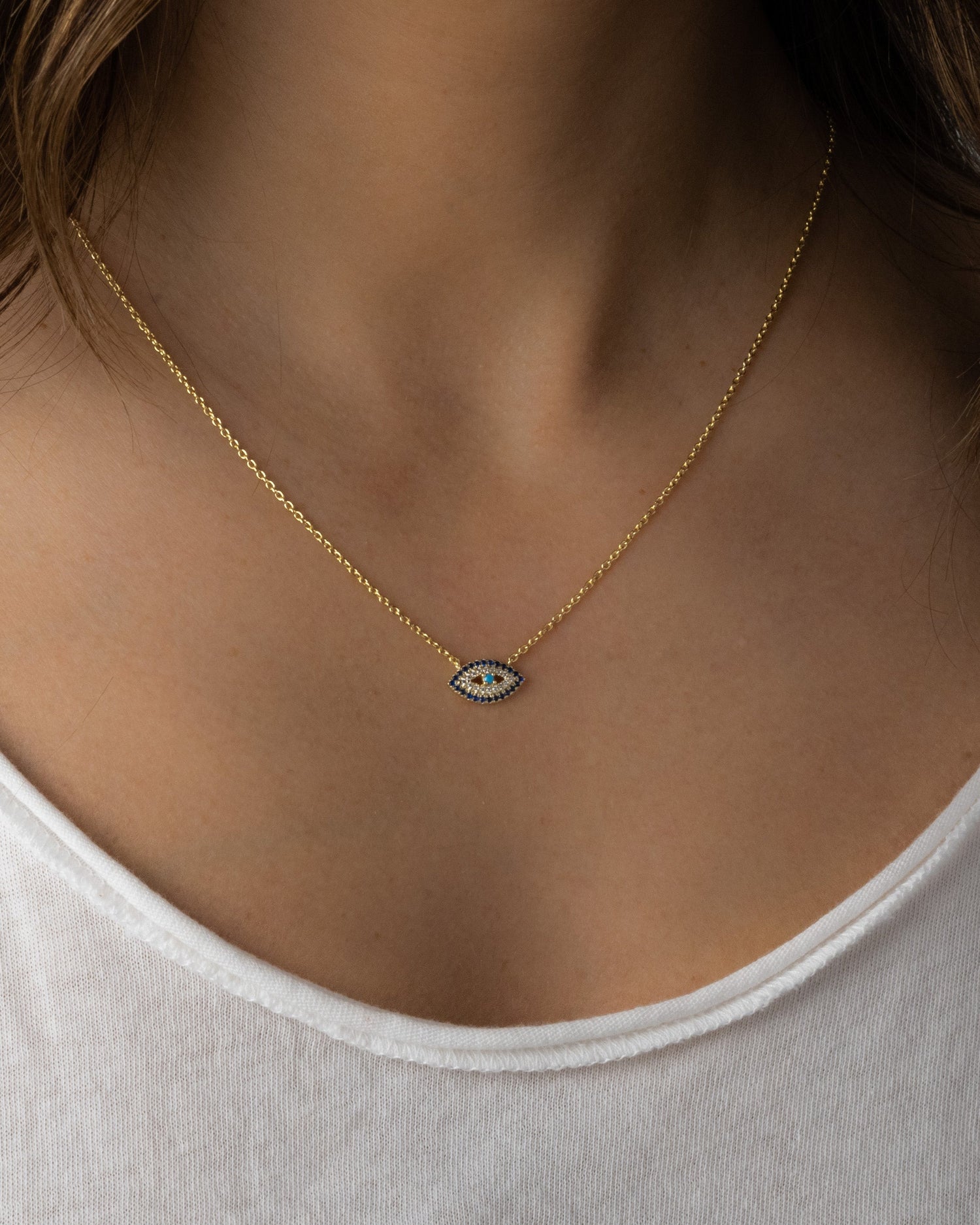 Model wearing gold chain necklace with evil eye pendant and sapphire diamonds