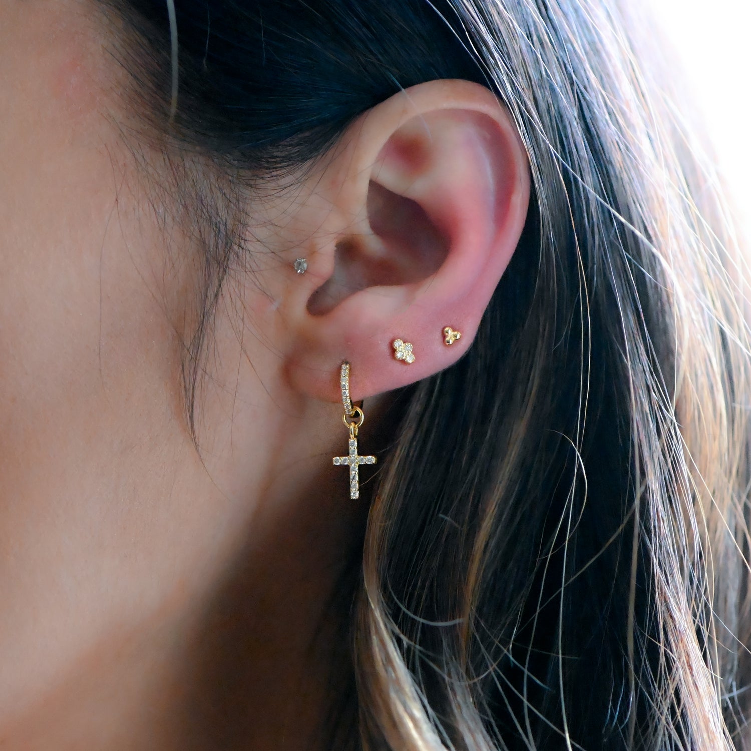 Model wearing gold pavé huggie earrings with removable cross charms and dainty gold studs in ear.