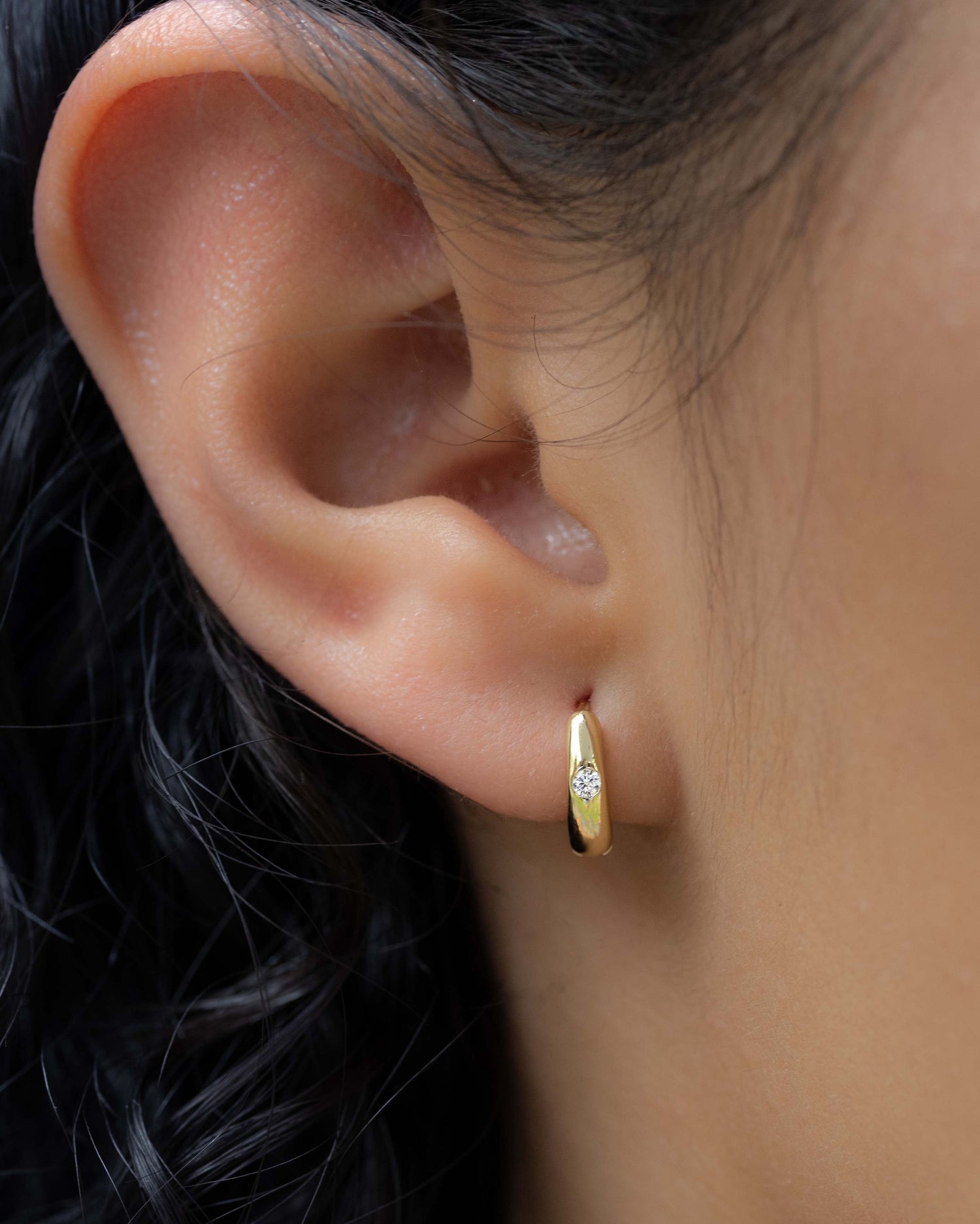 model wearing minimalist gold huggie hoop with small cz stone 
