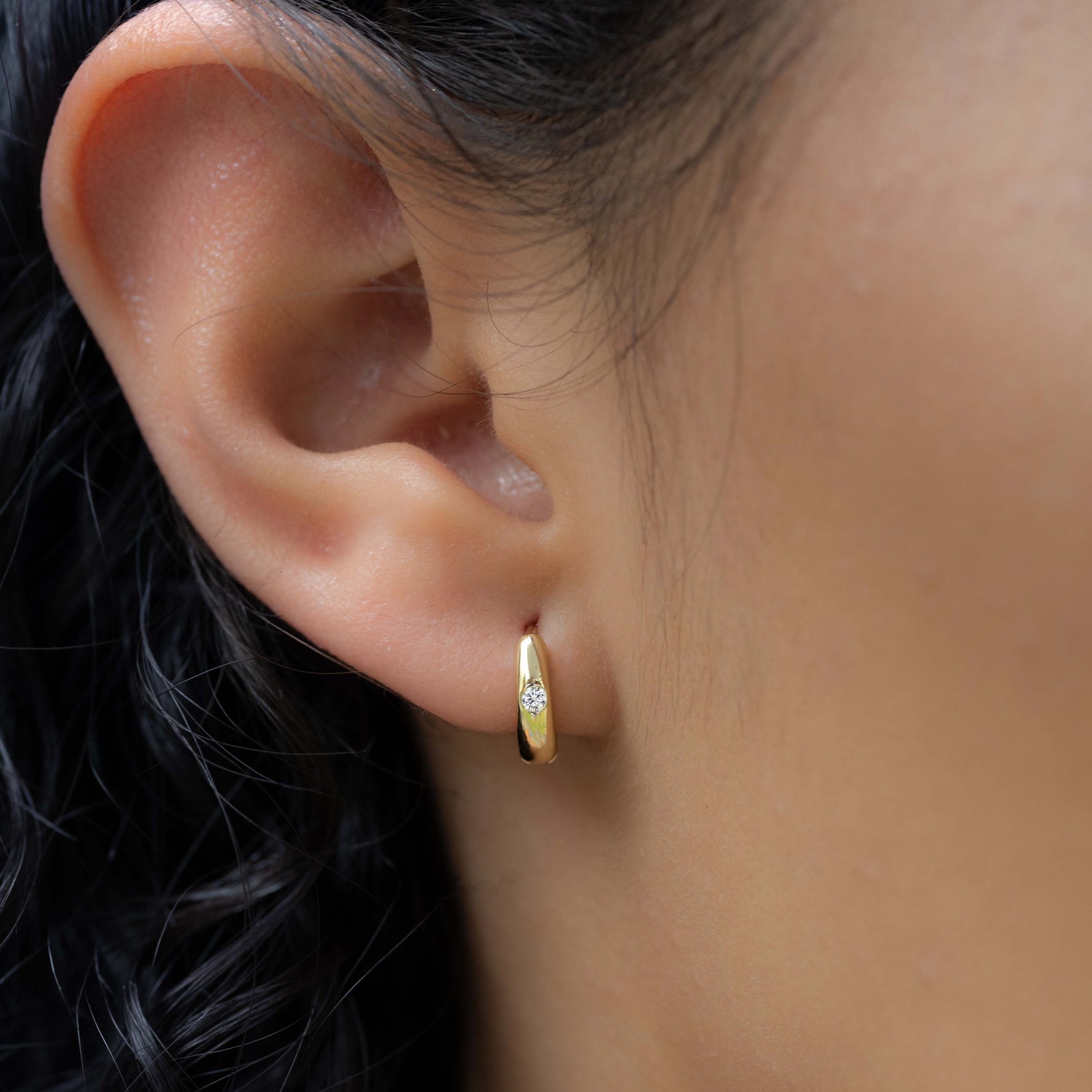 model wearing minimalist gold huggie hoop with small cz stone 