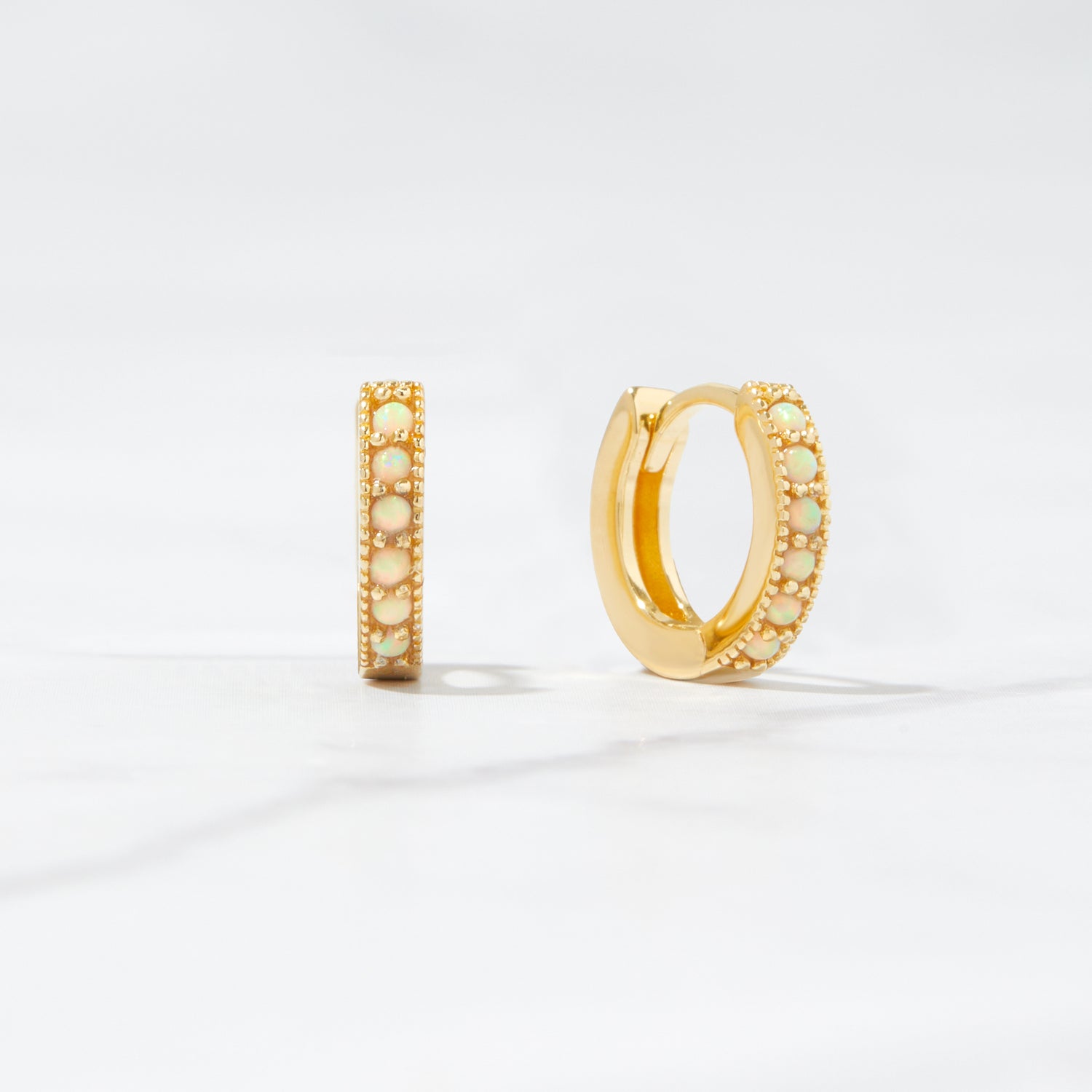 Close up flat-lay tiny hoop earrings. The huggie hoop earrings feature opal stones.