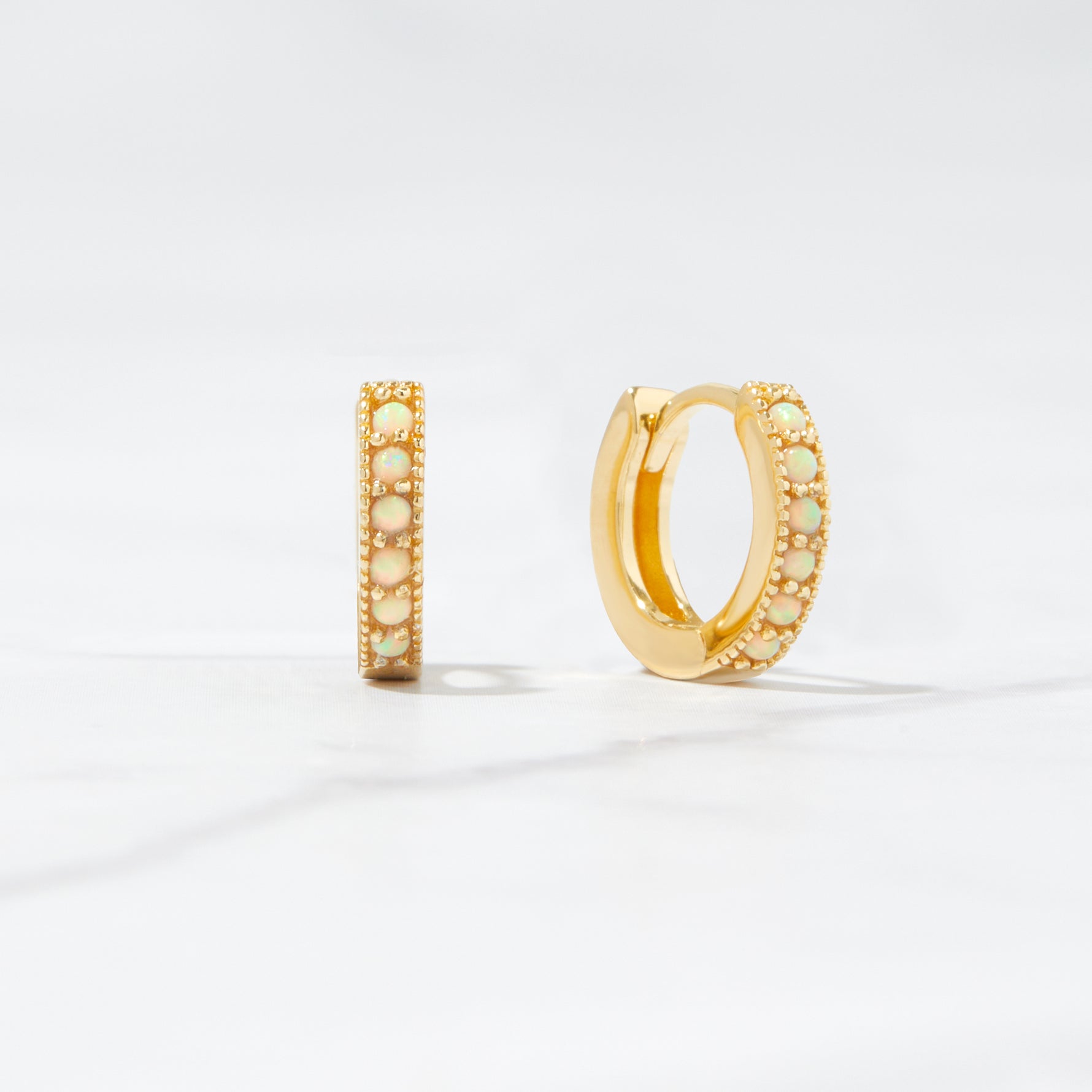 Close up flat-lay tiny hoop earrings. The huggie hoop earrings feature opal stones.