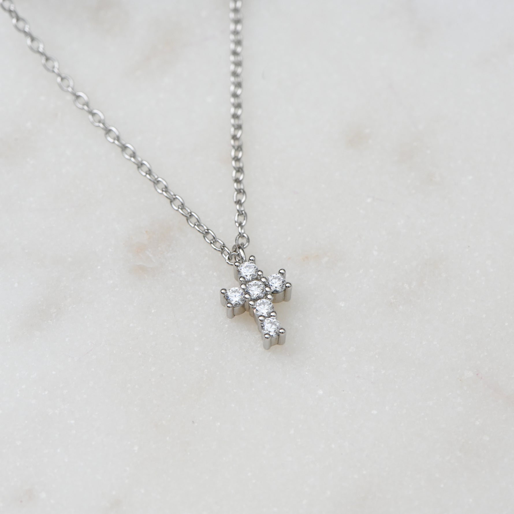 Silver tiny diamond cross necklace with chic, minimalist style showcased on white marble background