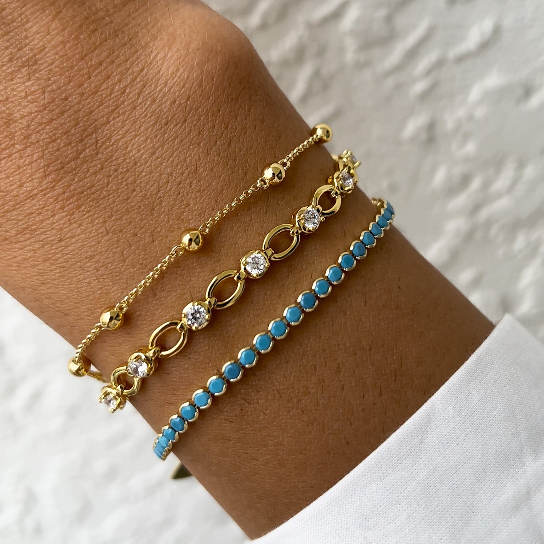 turquoise bracelet, tennis chain bracelet, and beaded ball bracelet on models arm